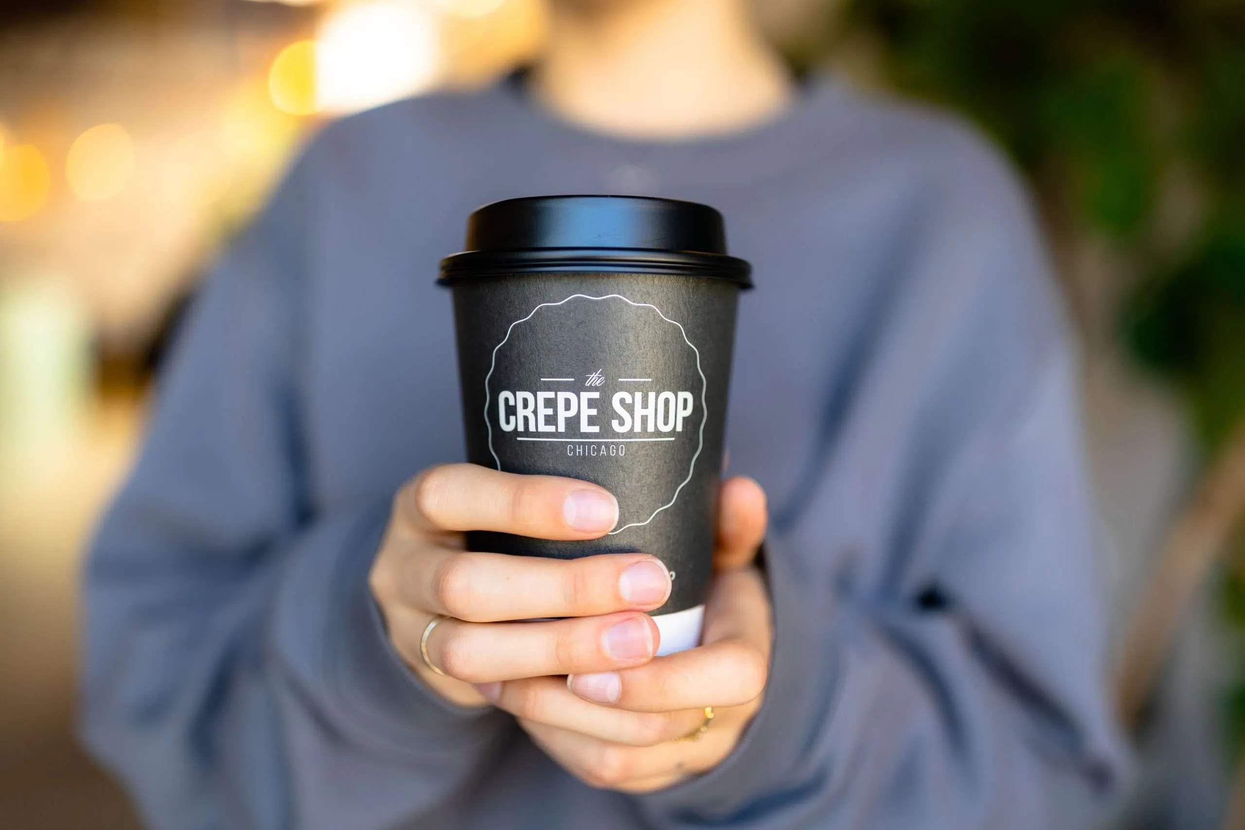 A coffee cup bearing The Crepe Shop Chicago logo