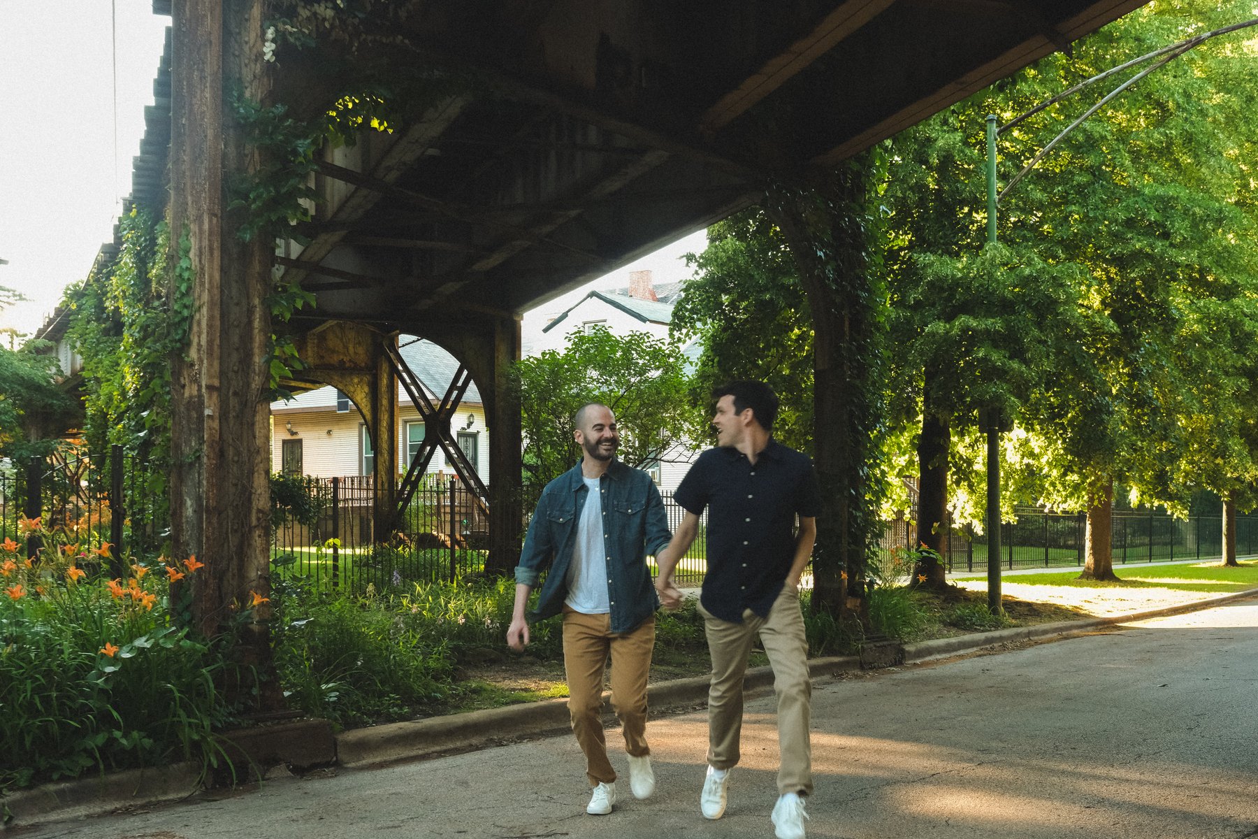 Jacob and Bradley walking together beneath the train tracks on a leafy Chicago street